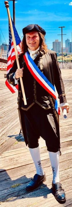 Jonathan Kruk dressed in 18th century style clothes, including a tri corner hat, and holding an American Flag